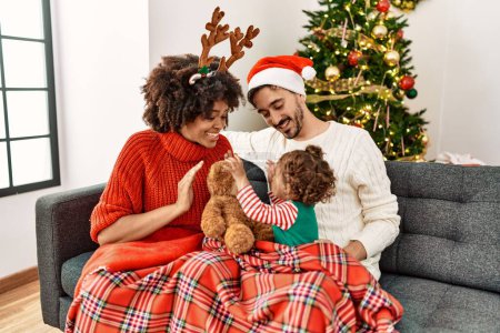 Photo for Couple and daughter playing with teddy bear sitting by christmas tree at home - Royalty Free Image
