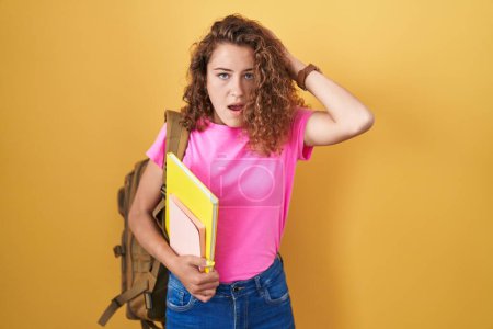 Photo for Young caucasian woman wearing student backpack and holding books crazy and scared with hands on head, afraid and surprised of shock with open mouth - Royalty Free Image