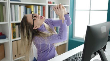 Téléchargez les photos : Jeune étudiante blonde utilisant une chanson de chant par ordinateur à la bibliothèque de l'université - en image libre de droit