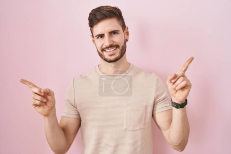 Téléchargez les photos : Homme hispanique avec la barbe debout sur fond rose souriant confiant pointant avec les doigts vers différentes directions. espace de copie pour la publicité - en image libre de droit