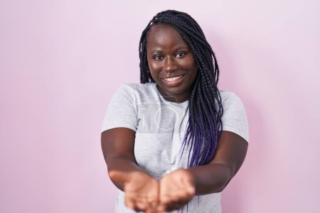 Photo for Young african woman standing over pink background smiling with hands palms together receiving or giving gesture. hold and protection - Royalty Free Image
