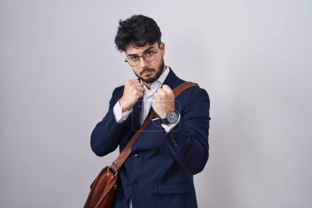 Téléchargez les photos : Homme hispanique avec barbe portant des vêtements de travail prêts à se battre avec geste de défense poing, visage en colère et contrarié, peur du problème - en image libre de droit