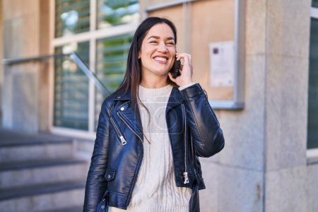Téléchargez les photos : Jeune femme souriant confiant parler sur le smartphone à la rue - en image libre de droit