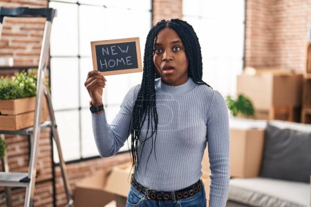 Photo for African american woman holding blackboard with new home text scared and amazed with open mouth for surprise, disbelief face - Royalty Free Image