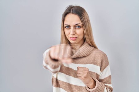 Photo for Young blonde woman wearing turtleneck sweater over isolated background punching fist to fight, aggressive and angry attack, threat and violence - Royalty Free Image