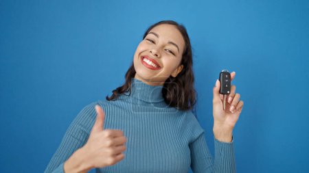 Photo for Young beautiful hispanic woman doing thumbs up holding key of new car over isolated blue background - Royalty Free Image