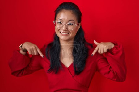 Photo for Asian young woman standing over red background looking confident with smile on face, pointing oneself with fingers proud and happy. - Royalty Free Image