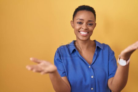 Foto de Mujer afroamericana de pie sobre fondo amarillo sonriente alegre ofreciendo manos dando asistencia y aceptación. - Imagen libre de derechos