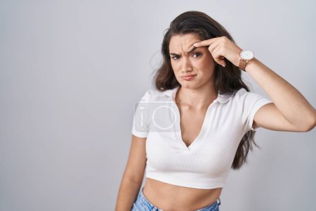 Photo for Young teenager girl standing over white background pointing unhappy to pimple on forehead, ugly infection of blackhead. acne and skin problem - Royalty Free Image
