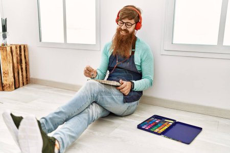 Téléchargez les photos : Young redhead man listening to music and drawing at art studio - en image libre de droit
