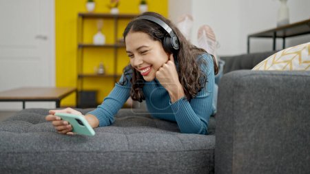Téléchargez les photos : Jeune belle femme hispanique regarder la vidéo sur smartphone couché sur le canapé à la maison - en image libre de droit