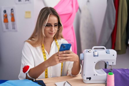 Téléchargez les photos : Young blonde woman tailor smiling confident using smartphone at clothing shop - en image libre de droit