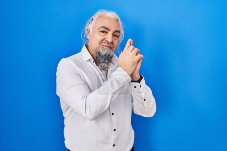 Photo for Middle age man with grey hair standing over blue background holding symbolic gun with hand gesture, playing killing shooting weapons, angry face - Royalty Free Image