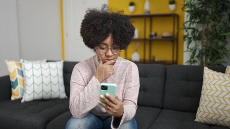 Foto de Mujer afroamericana joven usando teléfono inteligente estresado sentado en el sofá en casa - Imagen libre de derechos