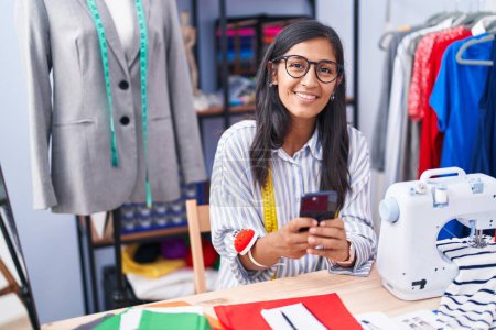 Photo for Young beautiful hispanic woman tailor smiling confident using smartphone at clothing factory - Royalty Free Image
