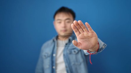 Foto de Joven chino haciendo stop gesture con la mano sobre fondo azul aislado - Imagen libre de derechos