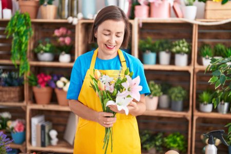 Téléchargez les photos : Femme d'âge moyen fleuriste tenant bouquet de fleurs à la boutique de fleurs - en image libre de droit