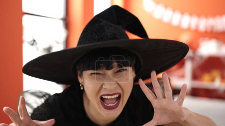 Téléchargez les photos : Jeune femme chinoise portant un costume de sorcière faisant geste effrayant à la maison - en image libre de droit
