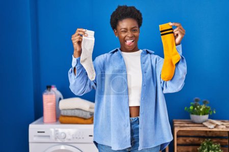 Téléchargez les photos : Afro-américaine femme tenant propre andy sale chaussettes coller langue dehors heureux avec drôle expression. - en image libre de droit