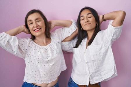 Téléchargez les photos : Mère et fille hispaniques ensemble relaxant et étirant, bras et mains derrière la tête et le cou souriant heureux - en image libre de droit