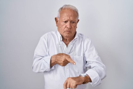 Foto de Hombre de edad avanzada con el pelo gris de pie sobre el fondo aislado en la prisa que apunta a ver el tiempo, la impaciencia, molesto y enojado por retraso plazo - Imagen libre de derechos