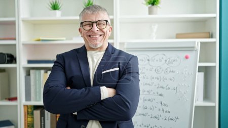 Photo for Middle age grey-haired man teacher smiling confident standing with arms crossed gesture by white board at university classroom - Royalty Free Image