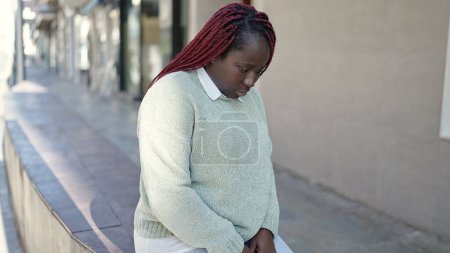 Téléchargez les photos : Femme africaine aux cheveux tressés debout avec une expression triste dans la rue - en image libre de droit