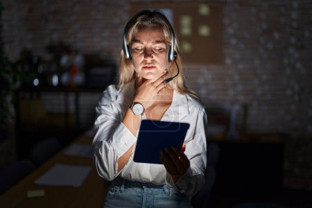 Téléchargez les photos : Jeune femme blonde travaillant au bureau la nuit touchant le cou douloureux, mal de gorge pour la grippe, la motte et l'infection - en image libre de droit