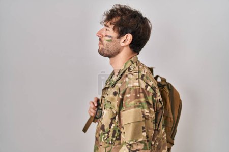 Photo for Hispanic young man wearing camouflage army uniform looking to side, relax profile pose with natural face and confident smile. - Royalty Free Image