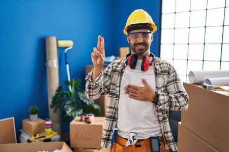 Photo for Young hispanic man with beard working at home renovation smiling swearing with hand on chest and fingers up, making a loyalty promise oath - Royalty Free Image