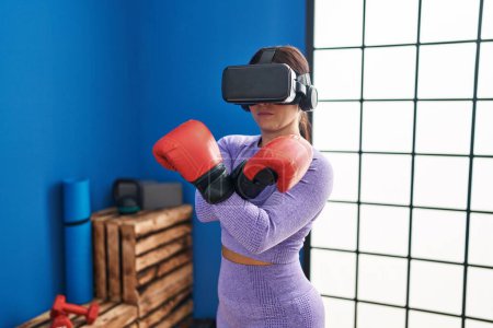 Téléchargez les photos : Jeune belle femme hispanique utilisant des lunettes de réalité virtuelle boxe au centre sportif - en image libre de droit