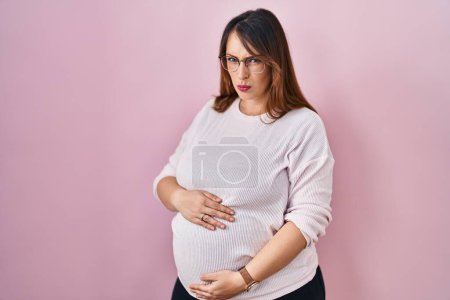 Foto de Mujer embarazada de pie sobre fondo rosa escéptico y nervioso, frunciendo el ceño molesto debido a un problema. persona negativa. - Imagen libre de derechos