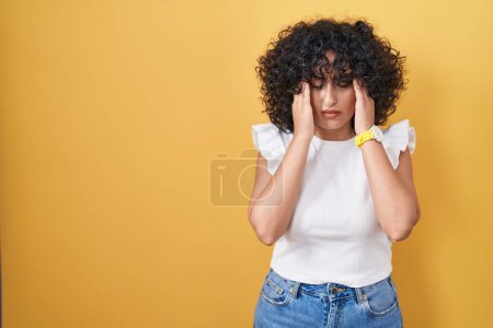 Photo for Young middle east woman standing over yellow background with hand on head for pain in head because stress. suffering migraine. - Royalty Free Image