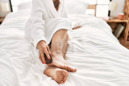 Photo for Middle age grey-haired woman massaging legs with cream sitting on bed at bedroom - Royalty Free Image