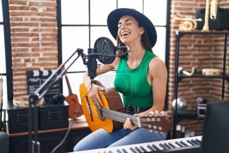 Téléchargez les photos : Young hispanic woman musician singing song playing classical guitar at music studio - en image libre de droit