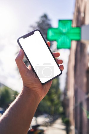 Téléchargez les photos : Homme tenant smartphone montrant écran blanc à la pharmacie - en image libre de droit