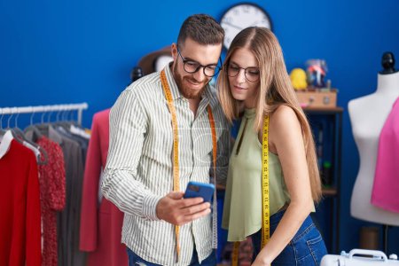 Téléchargez les photos : Man and woman tailors smiling confident using smartphone at clothing factory - en image libre de droit