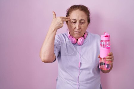 Photo for Senior woman wearing sportswear and headphones shooting and killing oneself pointing hand and fingers to head like gun, suicide gesture. - Royalty Free Image