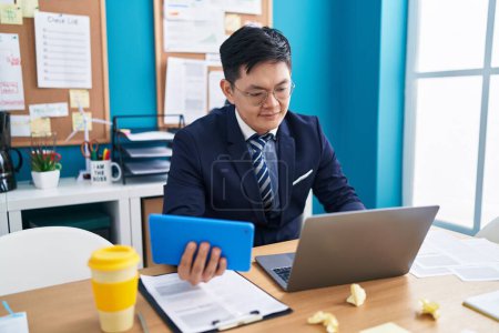 Téléchargez les photos : Jeune homme d'affaires chinois en utilisant le pavé tactile et l'ordinateur portable au bureau - en image libre de droit
