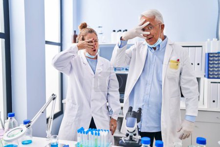Photo for Middle age hispanic people working at scientist laboratory peeking in shock covering face and eyes with hand, looking through fingers afraid - Royalty Free Image