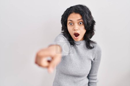 Photo for Hispanic woman with dark hair standing over isolated background pointing with finger surprised ahead, open mouth amazed expression, something on the front - Royalty Free Image