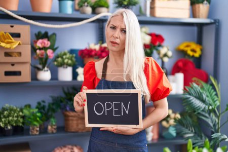 Photo for Caucasian woman working at florist holding open sign clueless and confused expression. doubt concept. - Royalty Free Image