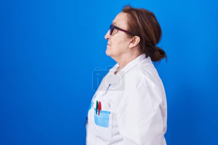 Photo for Senior woman with glasses wearing scientist uniform looking to side, relax profile pose with natural face with confident smile. - Royalty Free Image