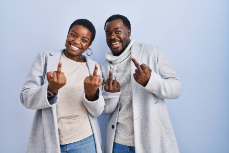Foto de Young african american couple standing over blue background together showing middle finger doing fuck you bad expression, provocation and rude attitude. screaming excited - Imagen libre de derechos