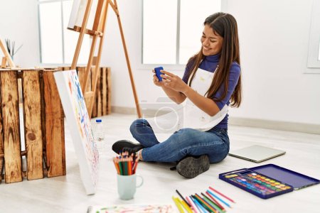Téléchargez les photos : Jeune femme latine faire une photo pour dessiner assis sur le sol au studio d'art - en image libre de droit