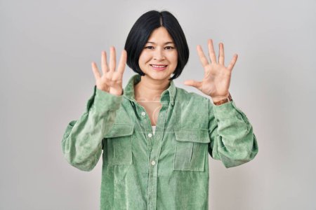 Foto de Joven mujer asiática de pie sobre fondo blanco mostrando y señalando hacia arriba con los dedos número nueve mientras sonríe confiado y feliz. - Imagen libre de derechos