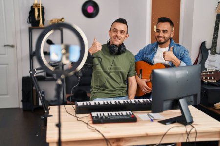 Photo for Two men playing classic guitar at music studio recording song smiling happy and positive, thumb up doing excellent and approval sign - Royalty Free Image