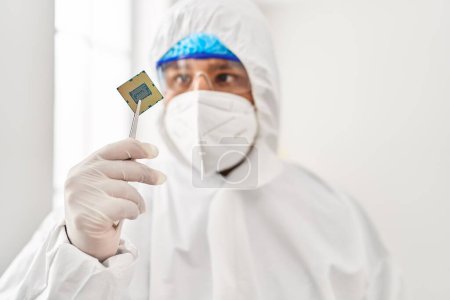 Foto de Joven científico latino usando uniforme de protección covid sosteniendo chip de procesador de CPU en el laboratorio - Imagen libre de derechos