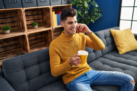 Téléchargez les photos : Jeune homme hispanique boire du café et parler sur le smartphone à la maison - en image libre de droit