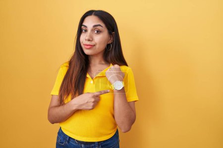 Photo for Young arab woman standing over yellow background in hurry pointing to watch time, impatience, looking at the camera with relaxed expression - Royalty Free Image